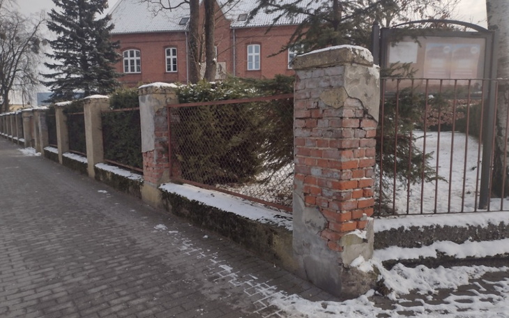 Zniszczony mur i ogrodzenie w zimowej scenerii.