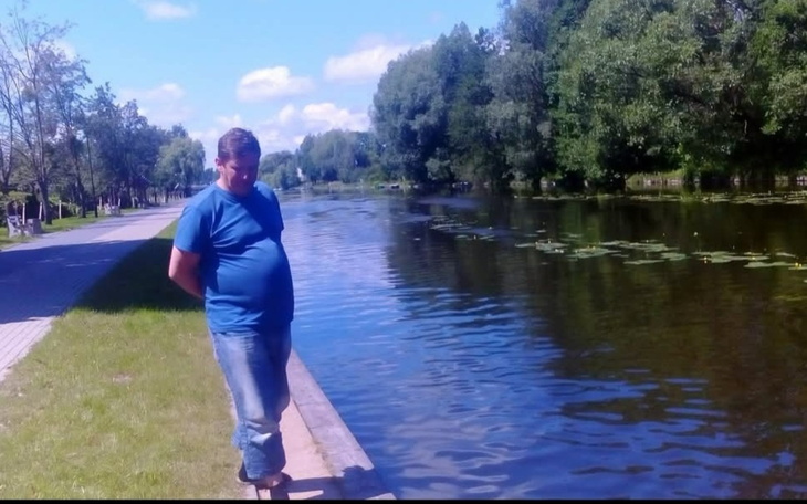 Mężczyzna stojący nad wodą, z rękami w kieszeniach.