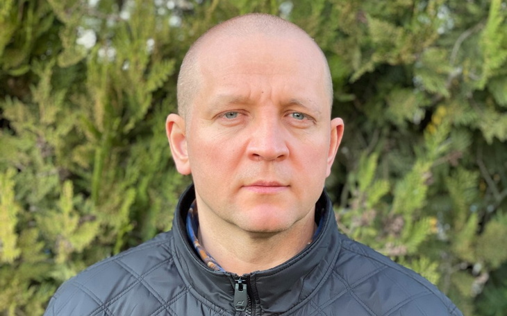 Mężczyzna w czarnej kurtce, stojący przed zielonym tłem.