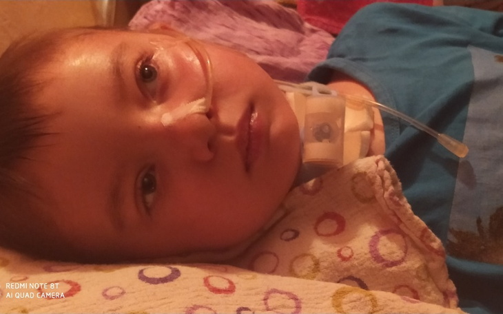 Chłopiec z rurką tlenową, leżący na poduszce w kolorowym otoczeniu.