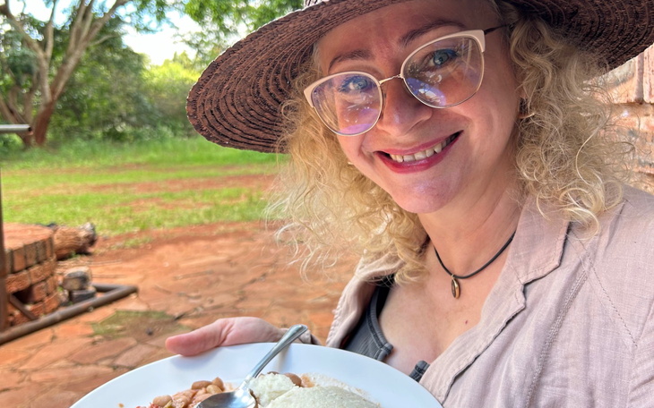 Kobieta w kapeluszu trzyma talerz z jedzeniem na tle zieleni.