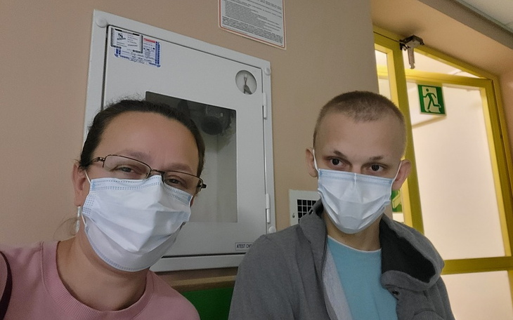 Dwie osoby w maseczkach, siedzące w szpitalnym korytarzu.