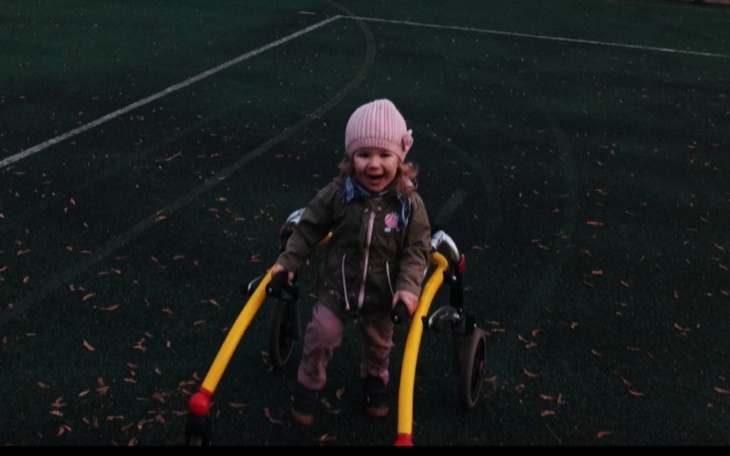 Mała dziewczynka uśmiechająca się na boisku, korzystająca z chodzika.