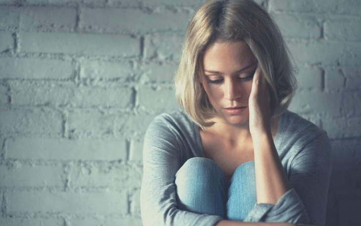 Kobieta siedząca na podłodze, zmartwiona i zamyślona.