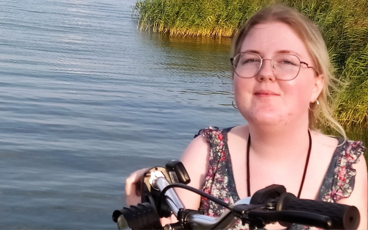 Młoda kobieta z rowerem nad wodą, uśmiechająca się w słońcu.