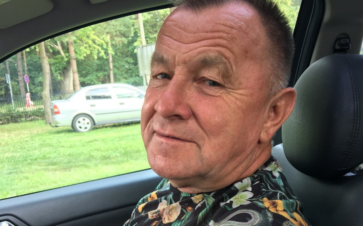 Mężczyzna w samochodzie, uśmiechający się do kamery.