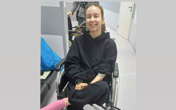 Młoda kobieta uśmiechająca się w wózku inwalidzkim, w szarym pomieszczeniu.