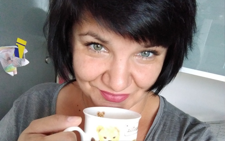 Kobieta trzymająca filiżankę, uśmiechająca się do kamery.