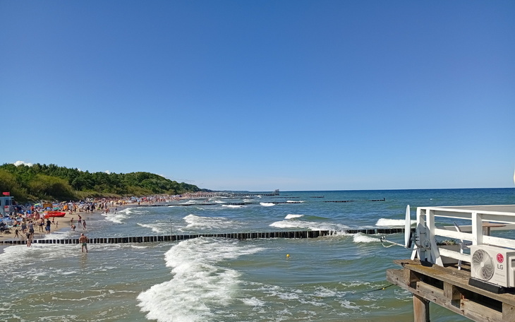 Plaża z falami i tłumem ludzi w słoneczny dzień.
