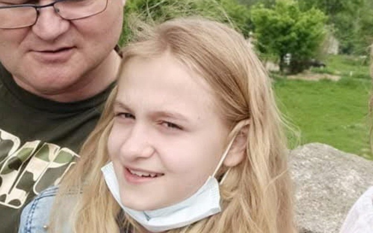 Portret dziewczynki z uśmiechem, w tle zieleń i bliskie osoby.