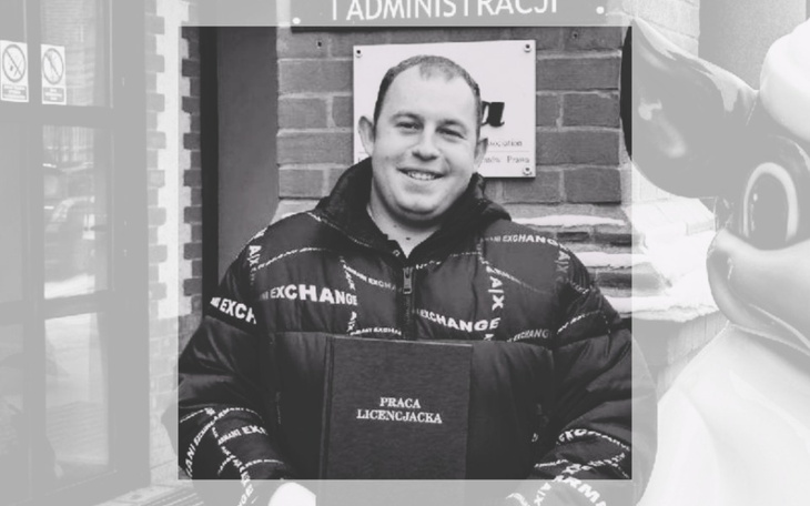 Mężczyzna trzymający dyplom, uśmiechający się do kamery.