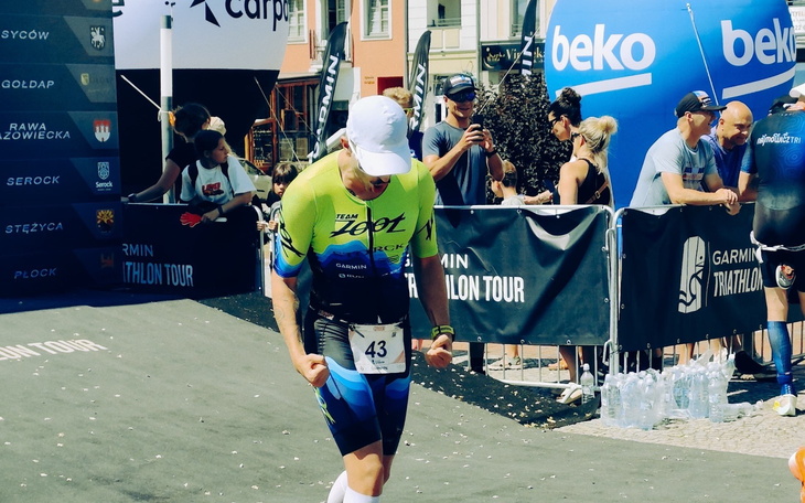 Zawodnik w stroju triathlonowym na mecie, w tle kibice.