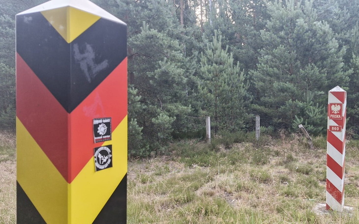 Słup graniczny z flagą Polski i Niemiec w lesie.