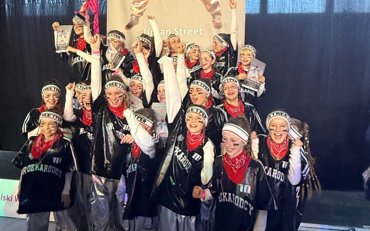 Grupa tancerzy w strojach, świętujących sukces na scenie.