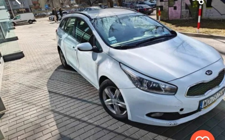 Biały samochód zaparkowany na chodniku, w tle widać budynki.