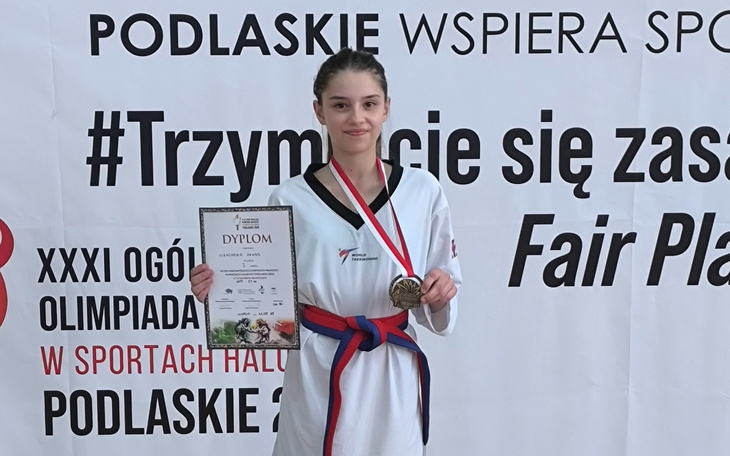 Młoda zawodniczka z dyplomem i medalem, dumnie prezentująca osiągnięcia.