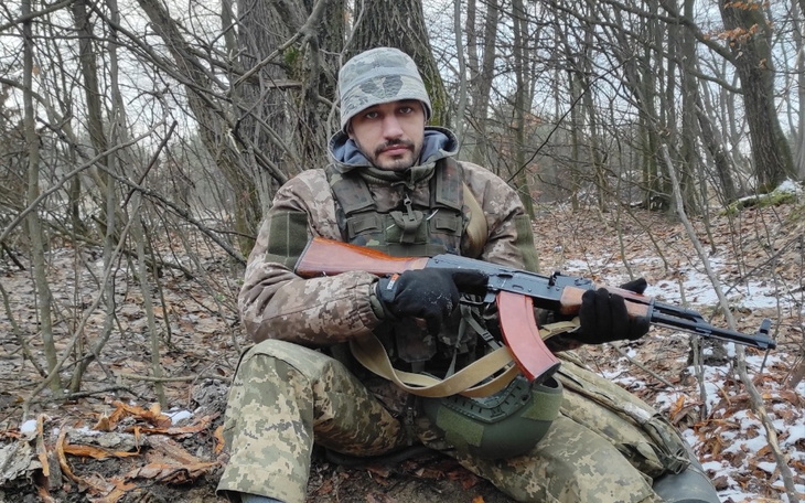 Mężczyzna w kamuflażu, siedzący w lesie z bronią.