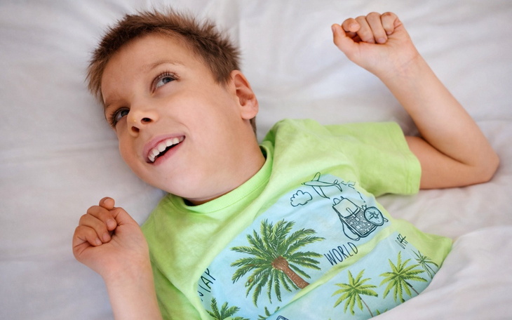 Chłopiec leży w łóżku, uśmiecha się i wygląda radośnie.
