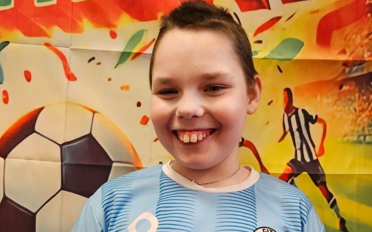 Uśmiechnięty chłopiec w koszulce piłkarskiej na tle kolorowej dekoracji.