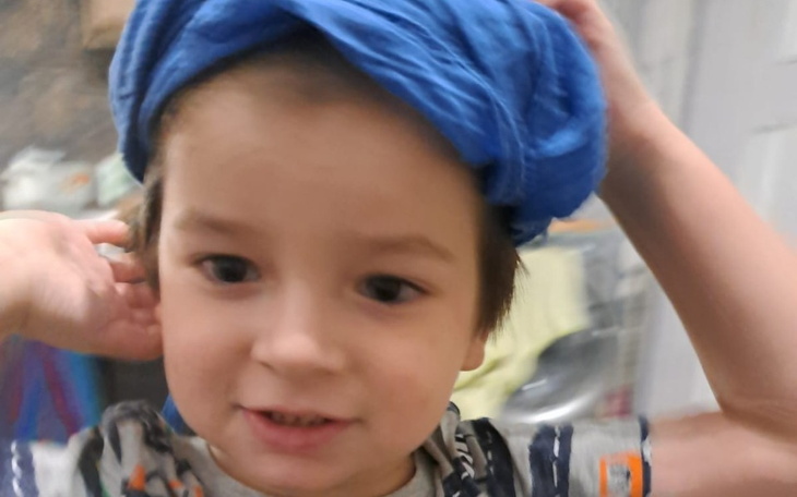 Chłopiec z niebieską chustą na głowie, uśmiechnięty i radosny.