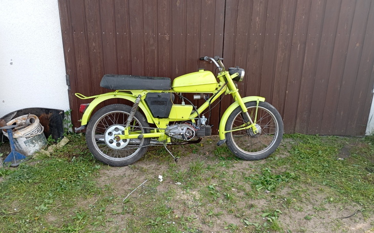 Stara motorynka w jaskrawym kolorze przy drewnianej bramie.