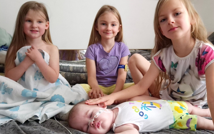 Trzy dziewczynki siedzące na łóżku, jedna z nich śpi.