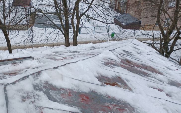 Zasypany śniegiem dach z widokiem na drzewa i ulicę.