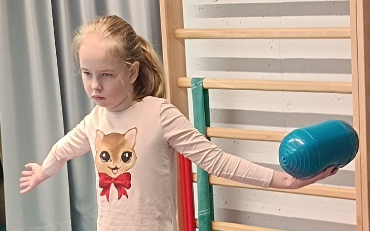 Dziewczynka ćwiczy równowagę z przedmiotem w ręku.