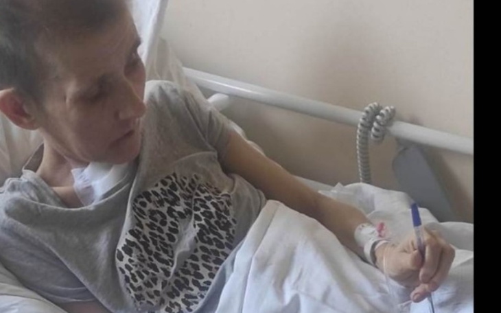 Chora kobieta leżąca w łóżku szpitalnym, pisząca coś na kartce.