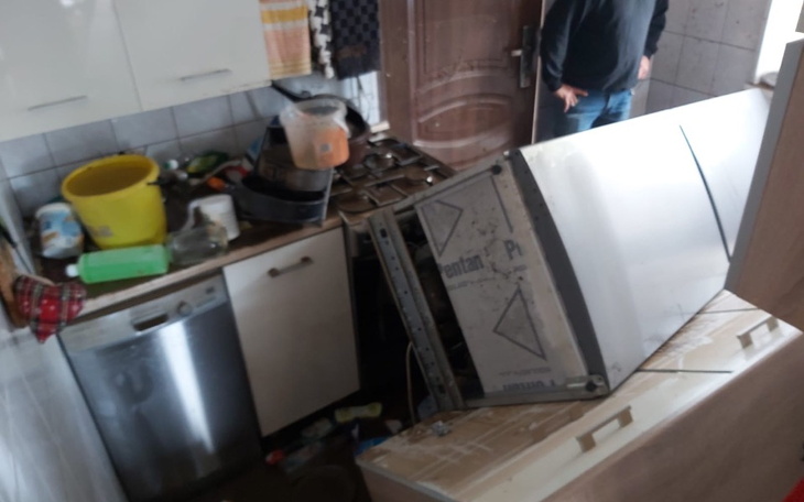 Zniszczona kuchnia z przewróconą lodówką i bałaganem.