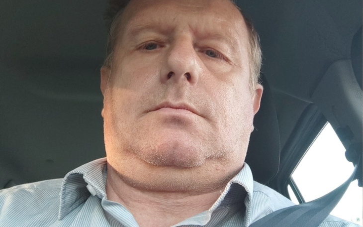 Mężczyzna w samochodzie, patrzy w obiektyw, poważny wyraz twarzy.