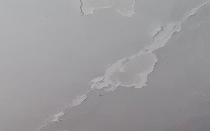 Uszkodzona farba na suficie, z widocznymi pęknięciami.