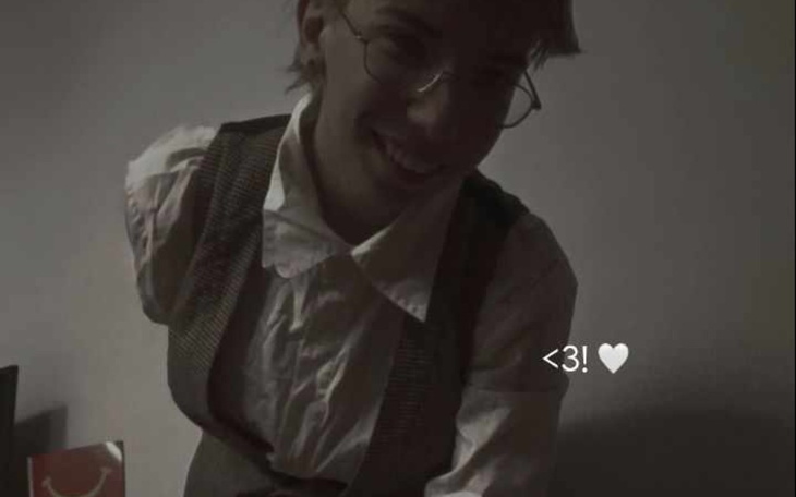 Osoba w okularach, uśmiechająca się w półmroku.