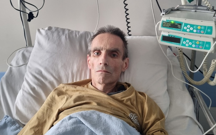 Mężczyzna leżący w łóżku szpitalnym, z poważnym wyrazem twarzy.