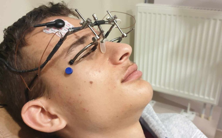 Młody mężczyzna z urządzeniem medycznym na głowie, leżący na łóżku.