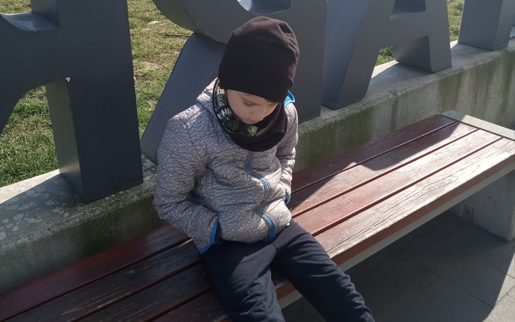 Chłopiec siedzący na ławce, z zamyśloną miną.