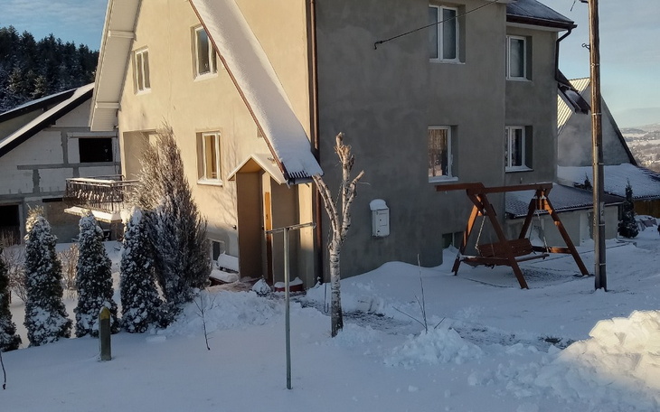 Zimowy krajobraz z domem i huśtawką w śniegu.