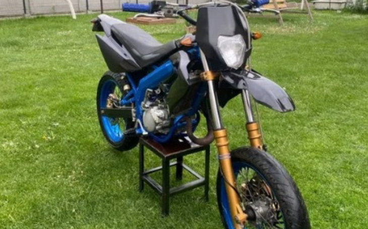 Motocykl na trawie, z niebieskimi akcentami i siedzeniem na krześle.