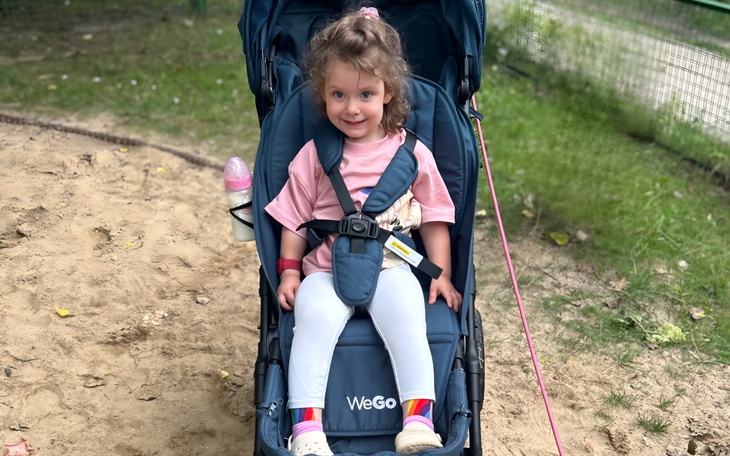 Mała dziewczynka siedząca w wózku dziecięcym na placu zabaw.