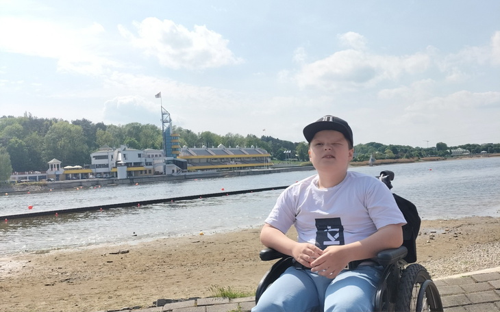 Chłopiec na wózku inwalidzkim nad jeziorem, w słoneczny dzień.