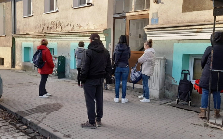 Ludzie stojący w kolejce przed budynkiem, przestrzegając dystansu.