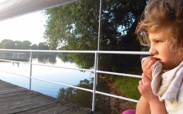 Dziewczynka siedząca na pomoście, zamyślona nad wodą.