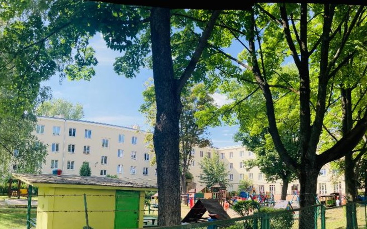 Widok na plac zabaw otoczony drzewami i budynkami.