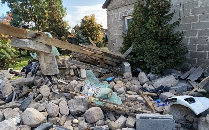 Zniszczony budynek z gruzem i roślinnością w tle.