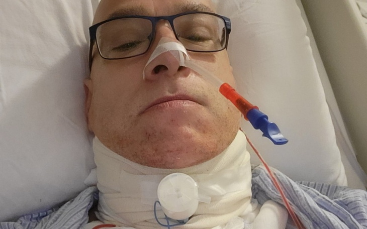 Mężczyzna w szpitalu, z rurką tlenową i opatrunkiem na szyi.
