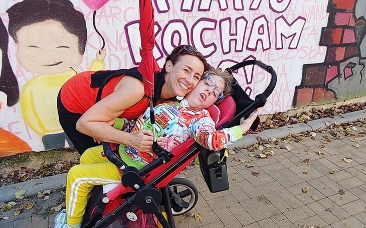 Kobieta z dzieckiem w wózku, pozująca przed muralem.