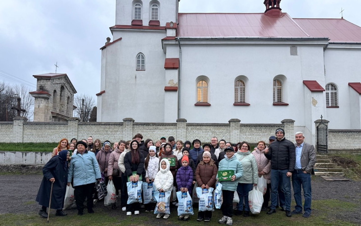 Zgromadzeni ludzie przed kościołem, zbiórka darów i uśmiechnięte twarze.