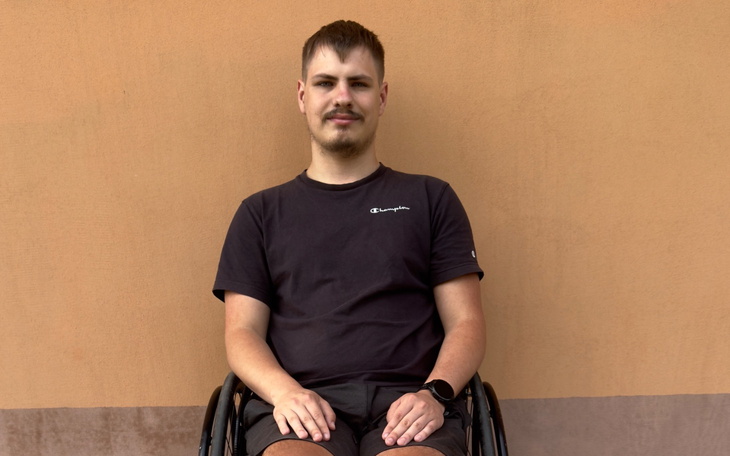 Mężczyzna na wózku inwalidzkim siedzący na tle ściany.