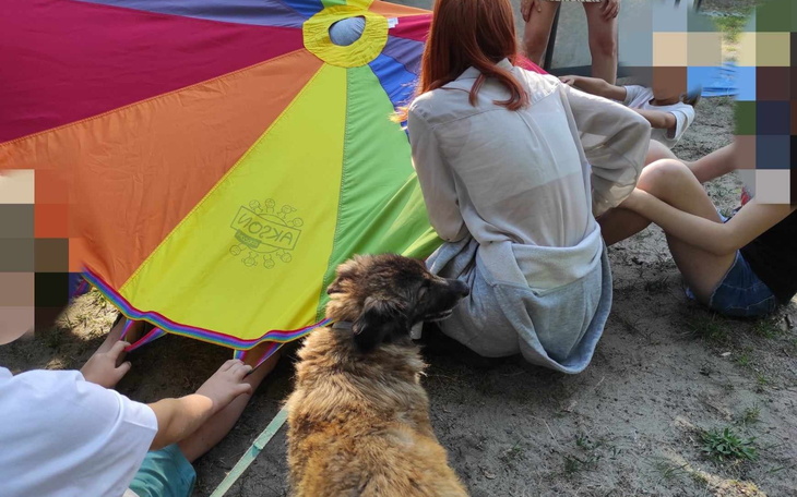 Grupa ludzi pod kolorowym parasolem, z psem w tle.