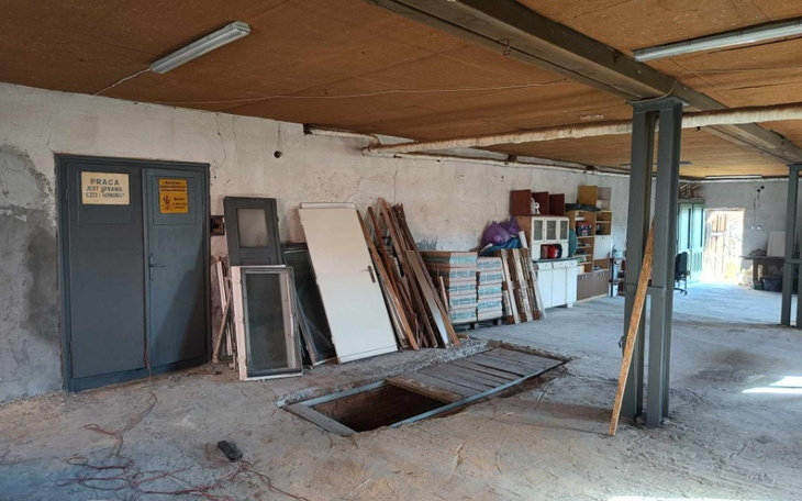 Wnętrze warsztatu z narzędziami i otwartym włazem.